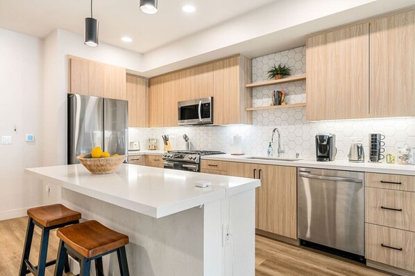 A modern kitchen with a central island, stainless steel appliances, wooden cabinets, and a white countertop.