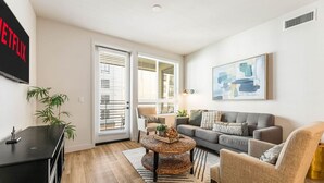 Un salon avec un canapé gris, une table basse ronde, un téléviseur et un tableau accroché au mur.