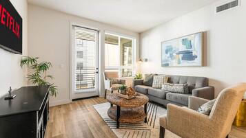 A living room with a grey sofa, a round coffee table, a TV, and a painting on the wall.