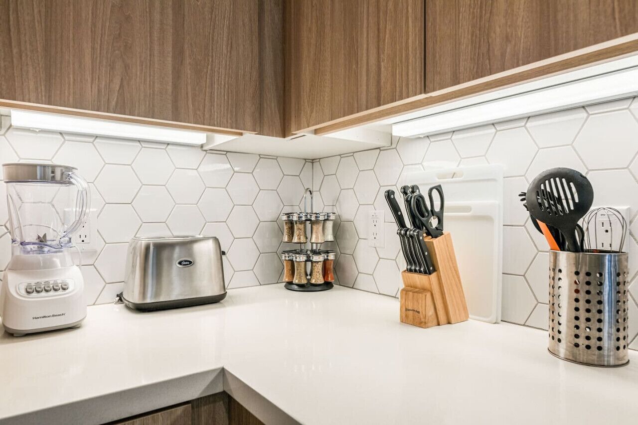 Une cuisine avec un plan de travail blanc, un mixeur, un grille-pain, un porte-épices et un porte-ustensiles.