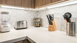 Une cuisine avec un plan de travail blanc, un mixeur, un grille-pain, un porte-épices et un porte-ustensiles.