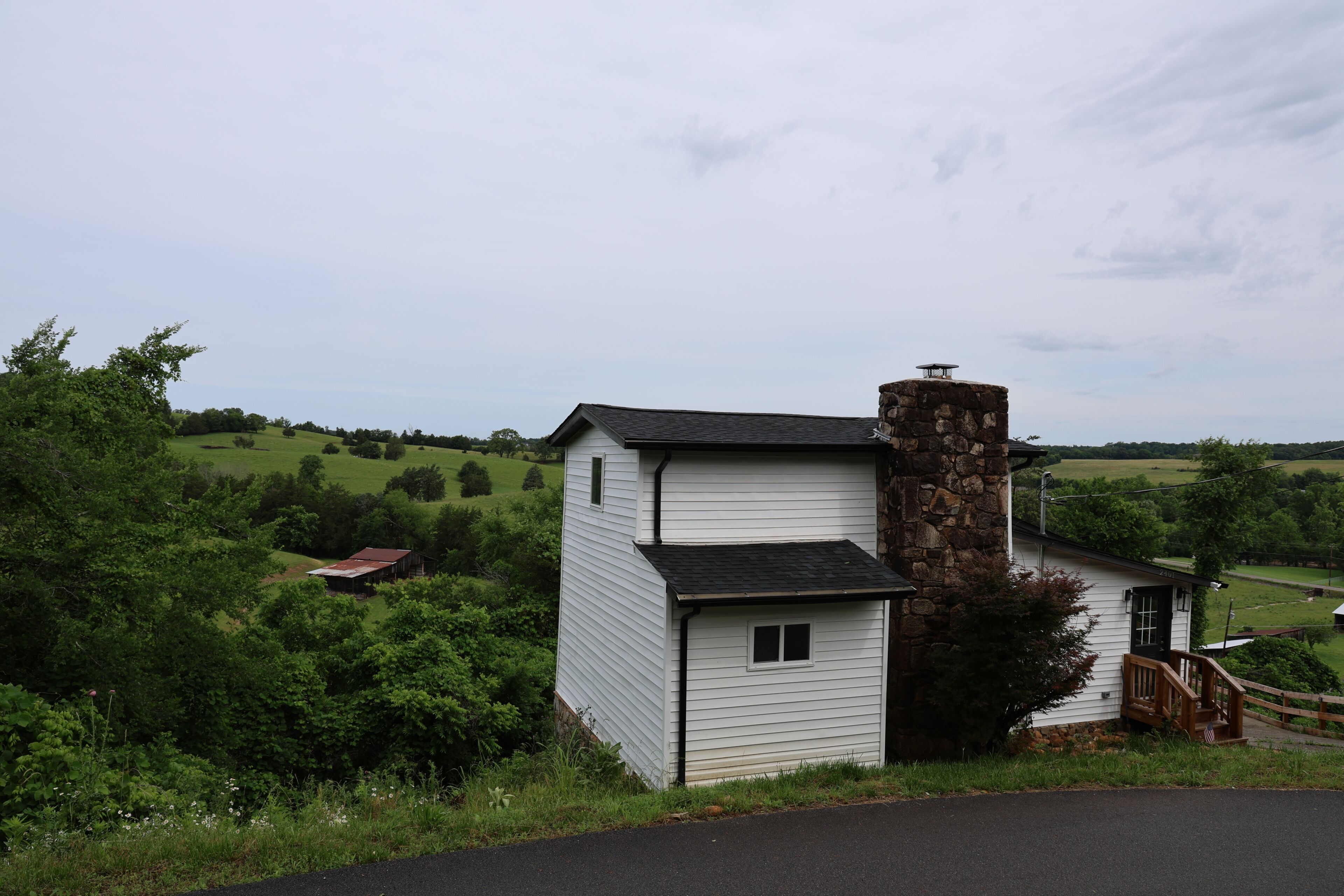 Un edificio blanco con chimenea de piedra, un porche de madera y vistas a un paisaje verde.