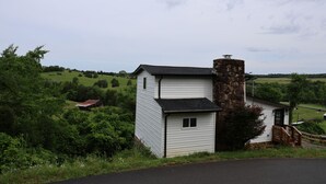 Un edificio blanco con chimenea de piedra, un porche de madera y vistas a un paisaje verde.