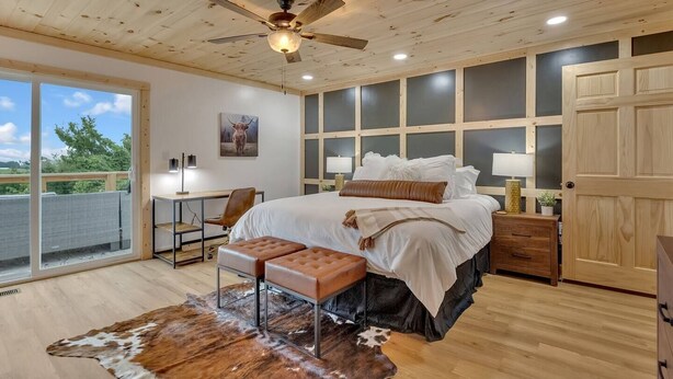 Un dormitorio con cama, escritorio, silla, ventilador de techo y un amplio ventanal.