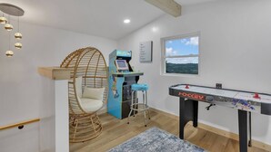 Una habitación con mesa de futbolín, consola de videojuegos, sillón colgante y ventana con vistas.