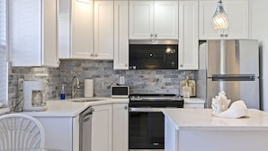 Uma cozinha moderna com armários brancos, forno embutido, geladeira de aço inoxidável e painel de backsplash de pedra.