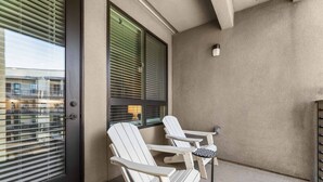 Un balcón con dos sillas Adirondack y una mesita, una puerta con ventanal, y una pared con textura.
