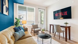 Una sala de estar con sofá, sillones, una mesa de centro, televisor y una planta.
