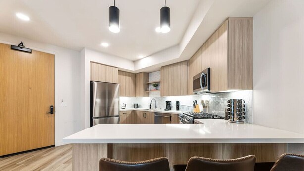 A modern kitchen with a central island, stainless steel appliances, and wooden cabinetry. - Chic & Cozy Condo | South Coast | Mins to Irvine (Santa Ana)