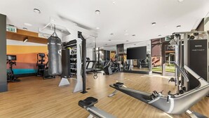 A modern gym with cardio machines, weightlifting equipment, and a punching bag. - Chic & Cozy Condo | South Coast | Mins to Irvine (Santa Ana)
