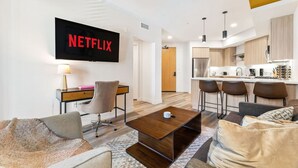 A modern living room with a sofa, coffee table, and a TV mounted on the wall displaying 'NETFLIX'. - Chic & Cozy Condo | South Coast | Mins to Irvine (Santa Ana)