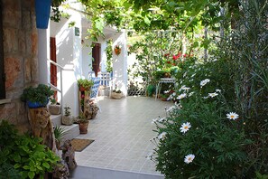 A courtyard with a tiled floor, potted plants, and a white building with red shutters. - Beautiful studio on ground floor in shadow of vines, Sveti Stefan (Sveti Stefan)