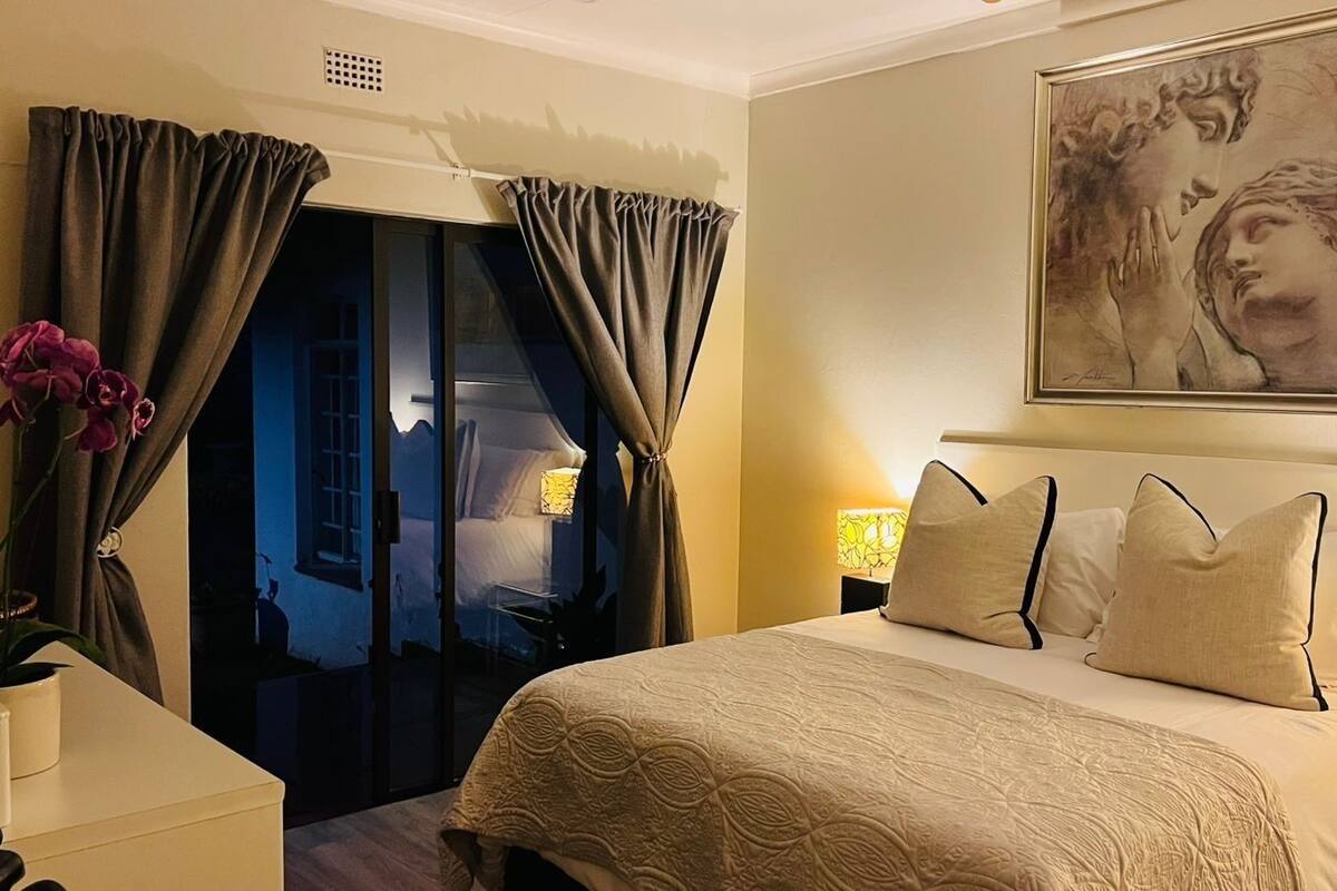 Een hotelkamer met een bed, gordijnen, een schilderij en een nachtkastje.