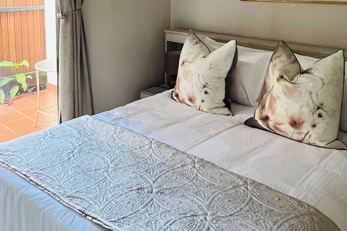 Een slaapkamer met een bed, gordijnen, een schilderij en uitzicht op de omgeving.
