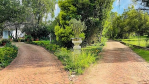 Een geplaveide tuinpad met een standbeeld in het midden, omringd door weelderige begroeiing en een hek.