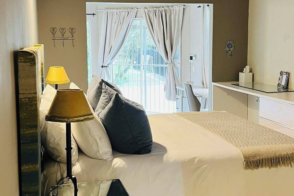 Een slaapkamer met een bed, een nachtkastje, een lamp, een raam met gordijnen, en een rieten plafond.