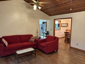 Ein Wohnzimmer mit einem roten Sofa, einem Holztisch und einem Deckenventilator.