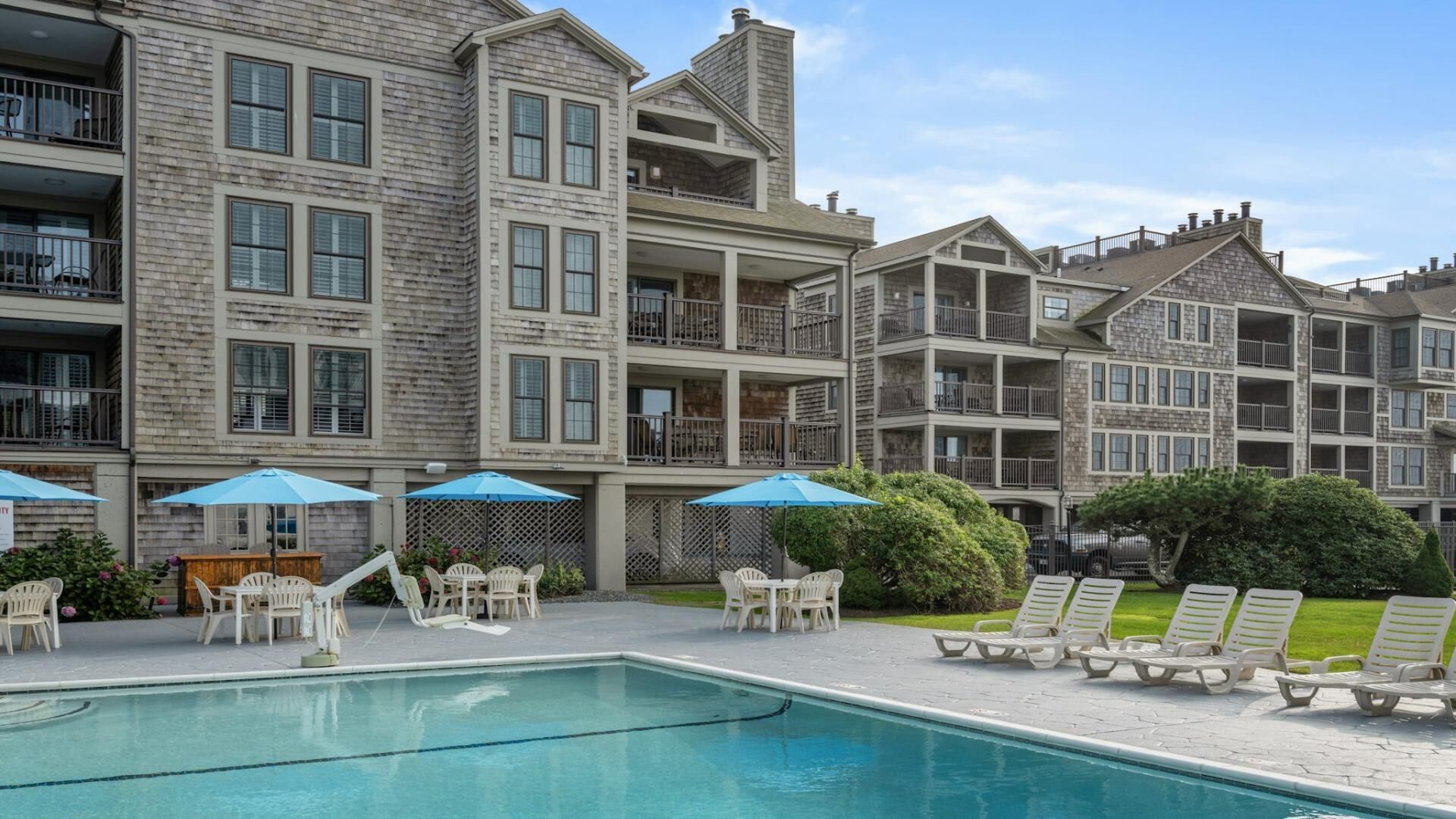 A multi-story hotel with a swimming pool, outdoor seating, and a well-maintained garden.