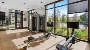 Ein modernes Fitnessstudio mit Cardiogeräten, Krafttrainingsgeräten und großen Fenstern mit Blick ins Freie.