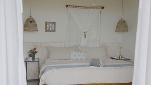 Un dormitorio con cama, mesitas de noche, lámpara colgante y ventana con cortinas.