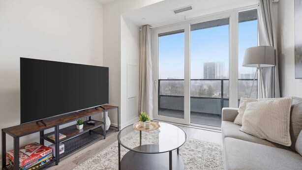 A modern living room with a flat-screen TV, a glass coffee table, a sofa, and a balcony with a view. - Contemporary Condo in DTK | Gym, Pool, & More (Kitchener)