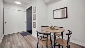 A room with a round wooden table, four chairs, a black door, and a wall-mounted mirror. - Contemporary Condo in DTK | Gym, Pool, & More (Kitchener)