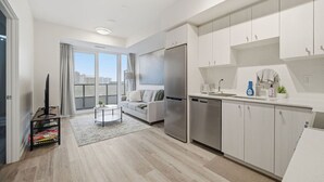 A modern kitchen with white cabinets, a stainless steel refrigerator, and a dining area with a table and chairs. - Contemporary Condo in DTK | Gym, Pool, & More (Kitchener)