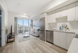 A modern kitchen with white cabinets, a stainless steel refrigerator, and a dining area with a table and chairs. - Contemporary Condo in DTK | Gym, Pool, & More (Kitchener)