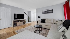 A modern living room with a sofa, TV, and a red curtain. - Spacious 3BR Upper Unit | Private Patio (Kitchener)