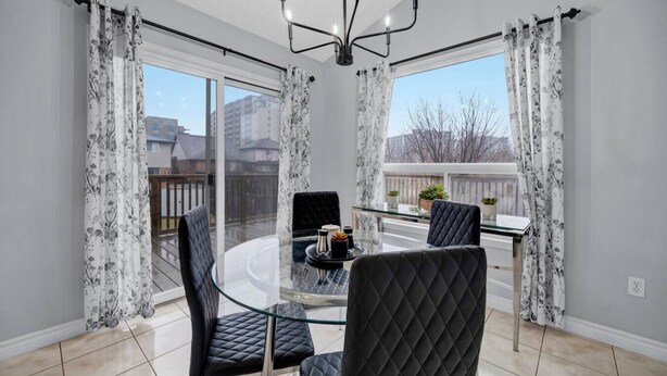 A modern dining area with a glass table, black cushioned chairs, and a chandelier. - Spacious 3BR Upper Unit | Private Patio (Kitchener)
