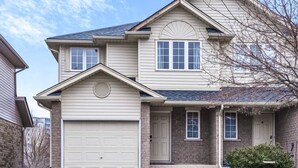 A two-story house with a garage, a brick facade, and a small porch. - Spacious 3BR Upper Unit | Private Patio (Kitchener)