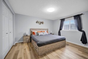 Une chambre à coucher avec un lit en bois, une table de chevet, une commode, une fenêtre avec des rideaux et un élément décoratif mural.