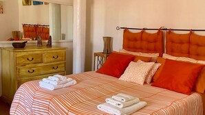 Un lit bien fait, avec une literie à rayures, une commode en bois dotée de tiroirs et un miroir.