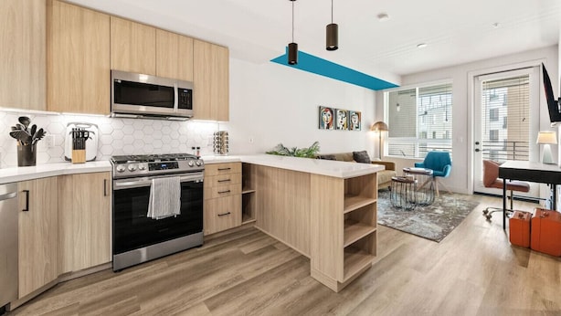 A modern kitchen with built-in appliances, a wooden countertop, and a dining area with a blue chair. - Bright & Modern Condo | 1Mi to South Coast Plaza (Santa Ana)