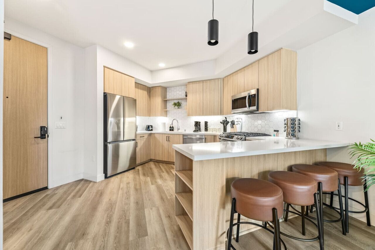 Una cucina moderna con mobili in legno, elettrodomestici in acciaio inossidabile, un'isola centrale con sgabelli e illuminazione a sospensione.