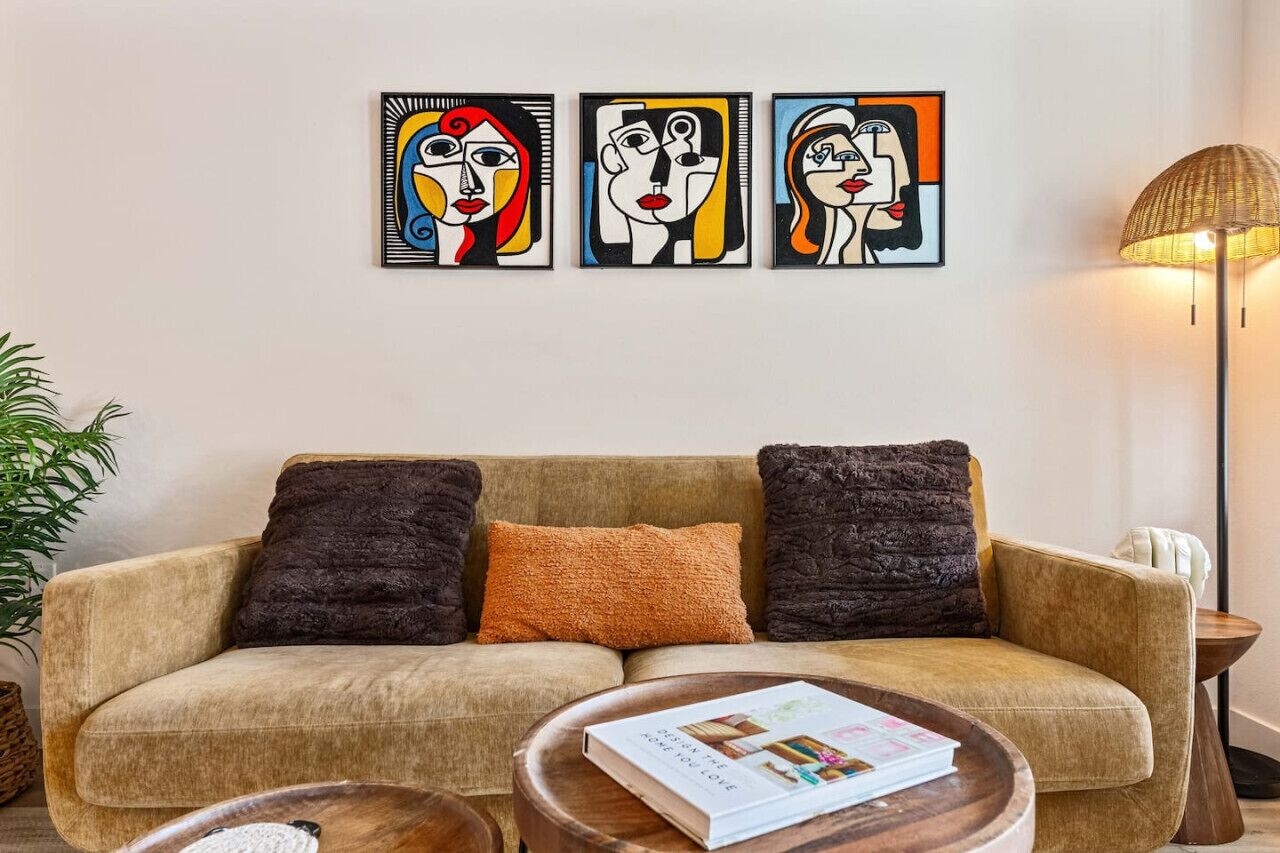 Un salon comprenant un canapé, trois coussins, une table basse avec un magazine, et trois tableaux abstraits accrochés au mur.
