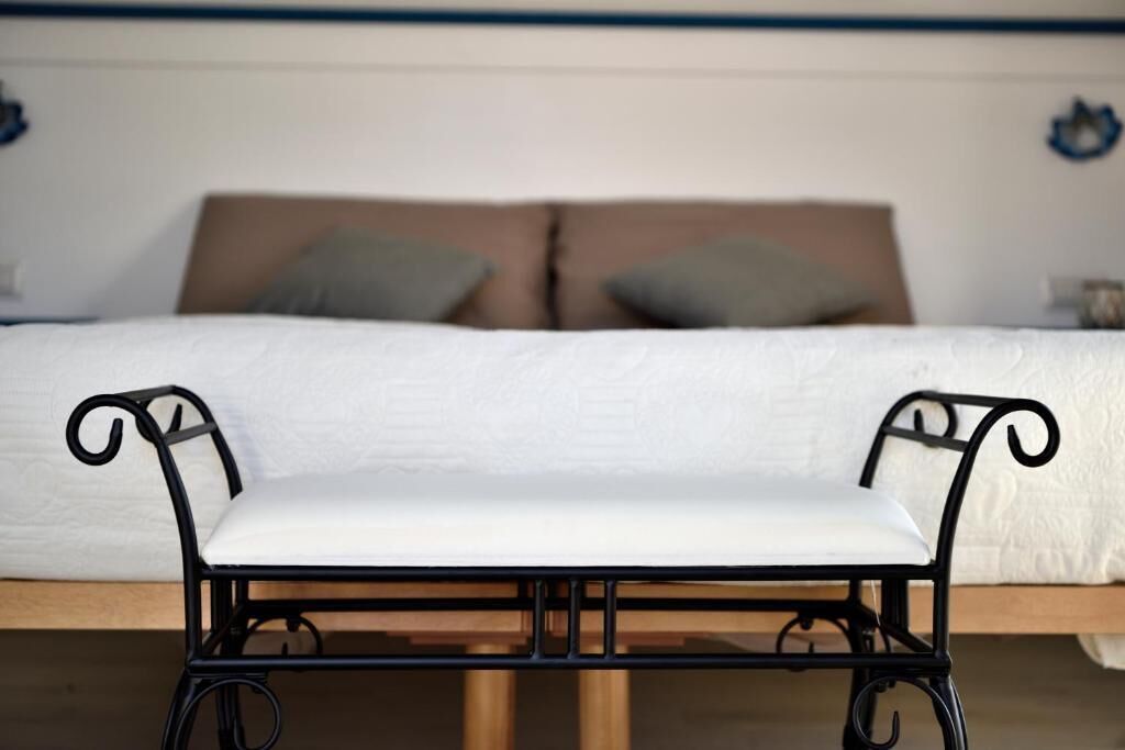 A bed with white bedding, two pillows, and a black metal bench in front.