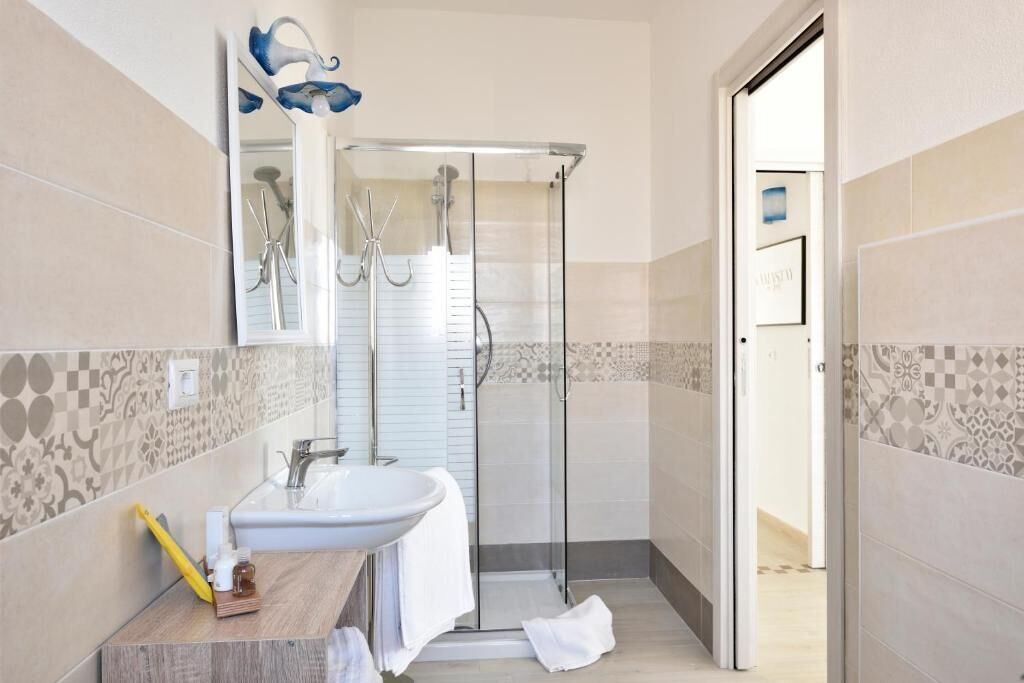 A bathroom with a glass shower enclosure, a sink, and a mirror.