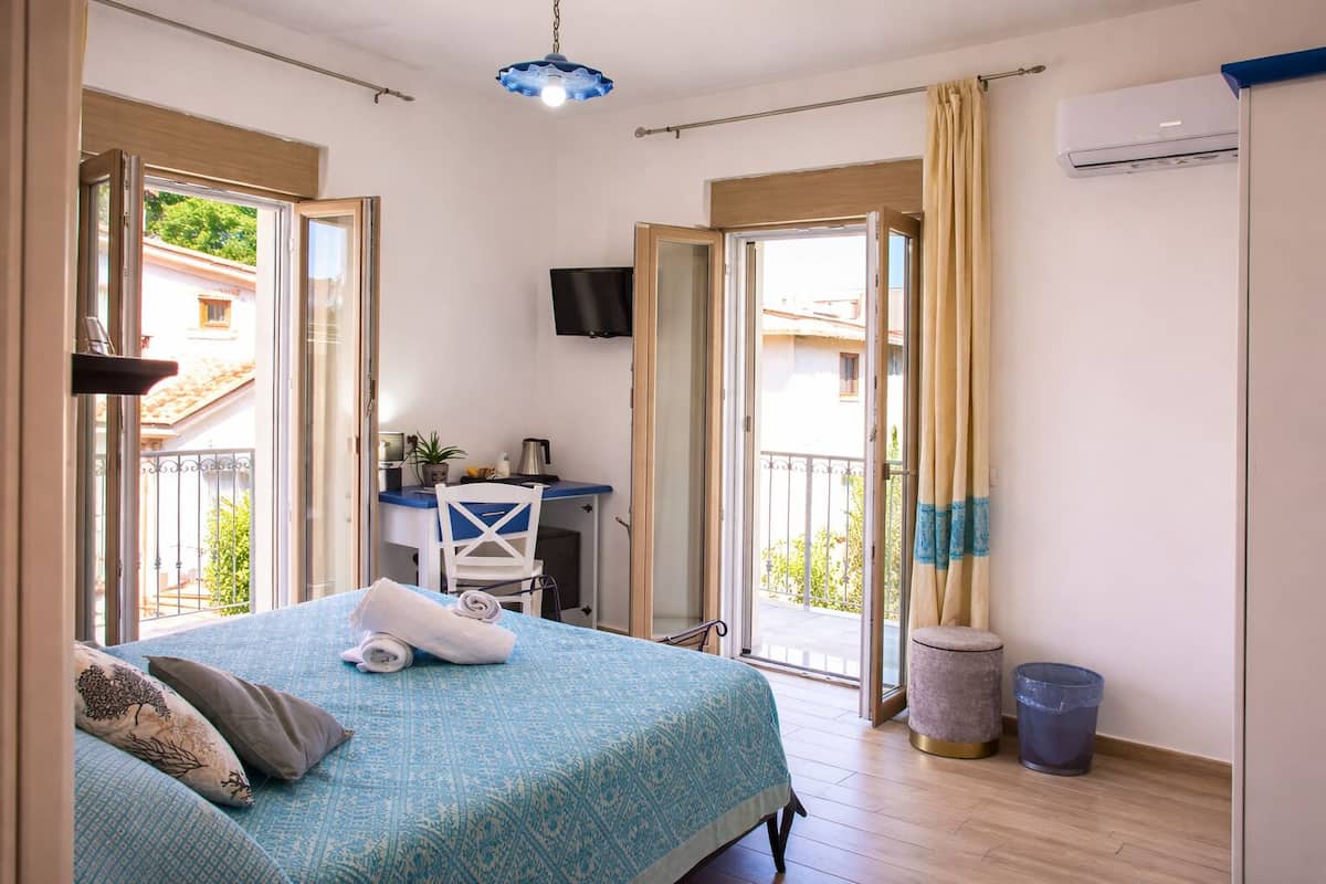 Une chambre avec un lit, un bureau, une chaise, une télévision et un balcon avec vue.