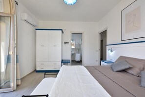 Un dormitorio con cama, armario, mesita de noche y baño visible a través de una puerta abierta.