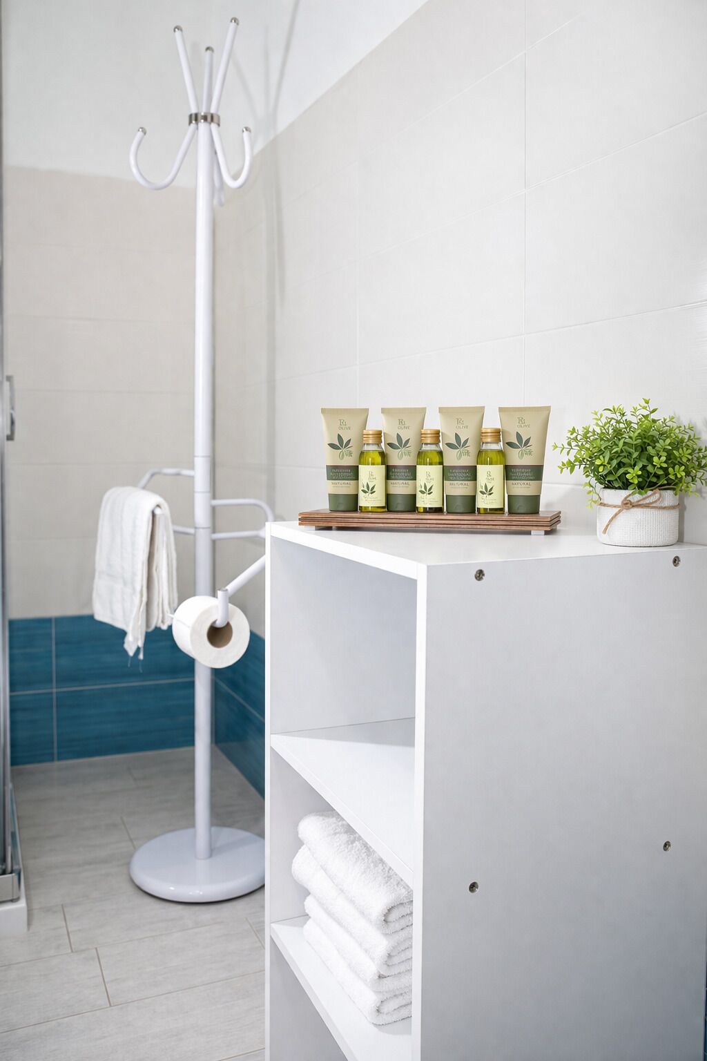 Een badkamer met een wit wastafelmeubel, een handdoekhouder, een plank met toiletartikelen en een potplant.