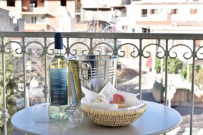Una botella de vino, una copa y una cesta con pasteles en una mesa de balcón.