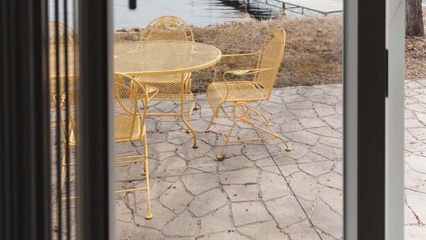 Vista attraverso una porta di vetro su un patio con tavolo e sedie, un molo e una distesa d'acqua.