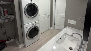 Una cucina moderna con lavatrice e asciugatrice integrate, un lavandino grande e una porta che dà su un'altra stanza.