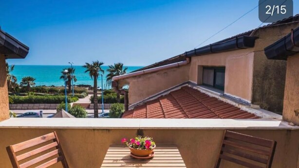 A balcony with a view of the sea, a wooden table with a flower pot, and two wooden chairs. - Waterfront Apartment in San Leone with Sea View (San Leone)