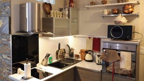 Eine moderne Küche mit einer Edelstahl-Dunstabzugshaube, einer Mikrowelle und einem Backofen. Regale mit dekorativen Gegenständen und eine Backsteinwand sind ebenfalls vorhanden.