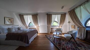 Un dormitorio con cama, dos sillas, una mesa y ventanas amplias con cortinas.