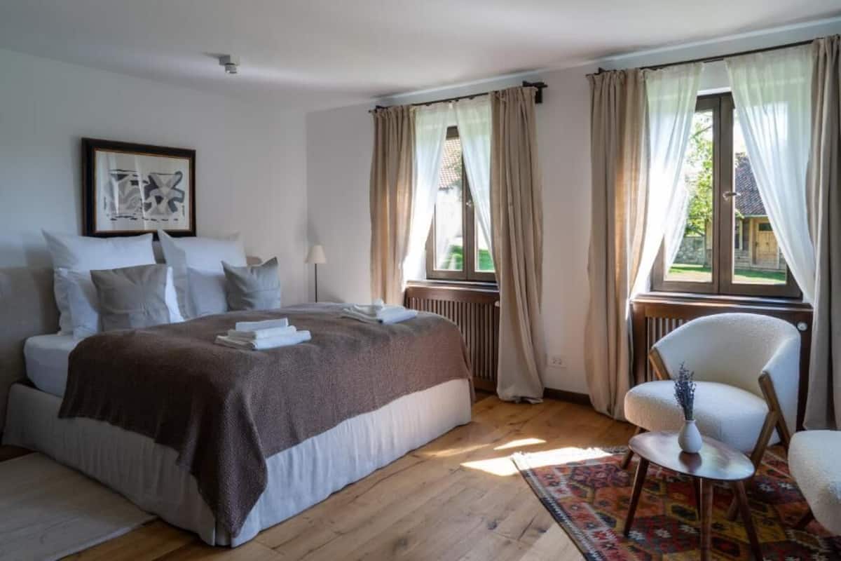 Una camera da letto con un letto, una sedia, un termosifone e una finestra con tende.