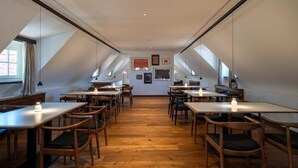 Un espace repas avec des tables et des chaises en bois, un plafond haut doté de lucarnes et des œuvres d’art accrochées aux murs.