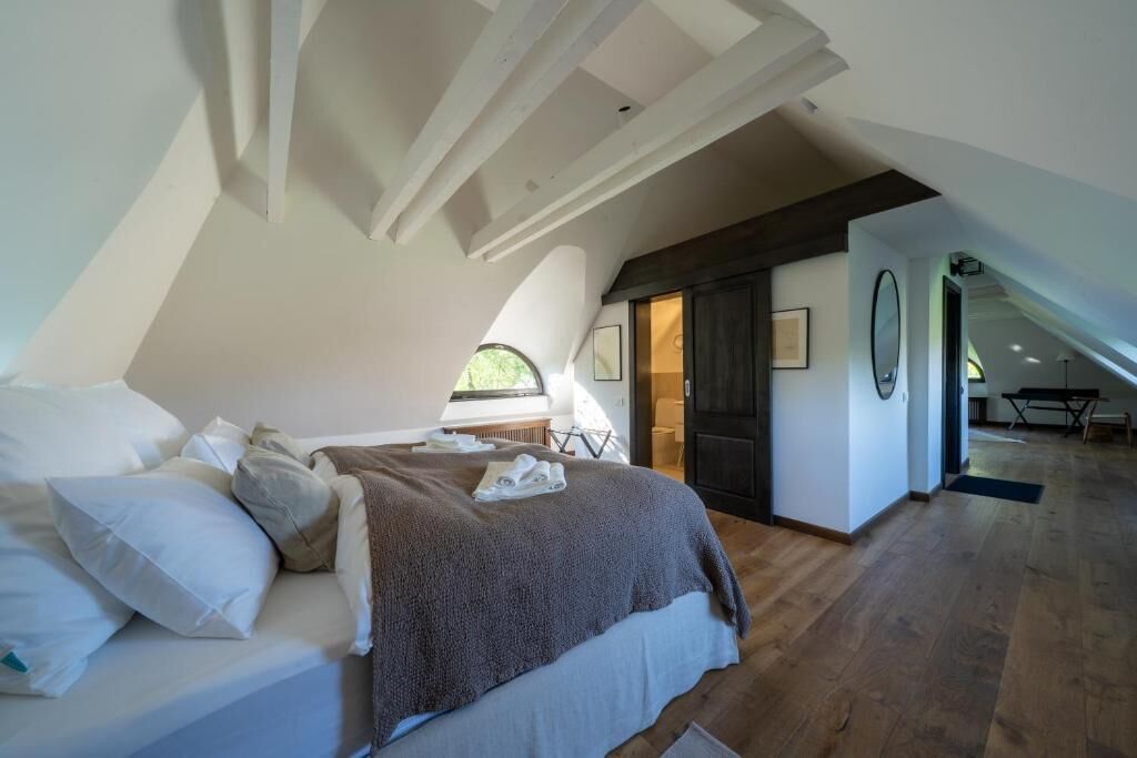 Quarto com teto inclinado, cama com almofadas e manta, e janela.